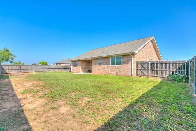 rear view of house with a fenced backyard, a lawn, and brick siding