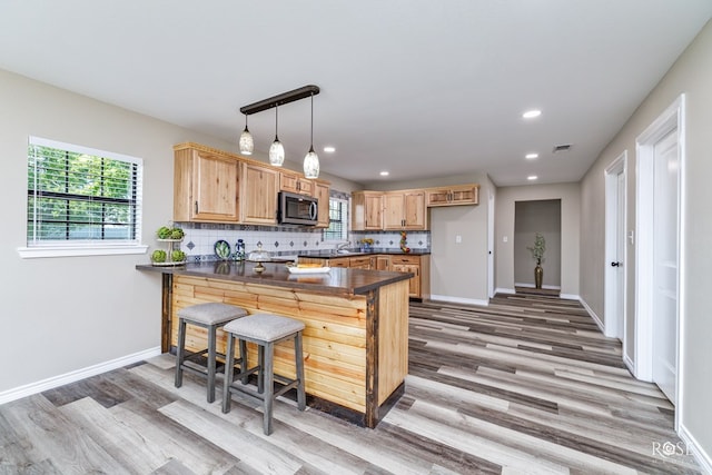 kitchen with hanging light fixtures, tasteful backsplash, a kitchen bar, kitchen peninsula, and light wood-type flooring