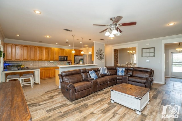 living room with ceiling fan with notable chandelier, ornamental molding, and light wood-type flooring