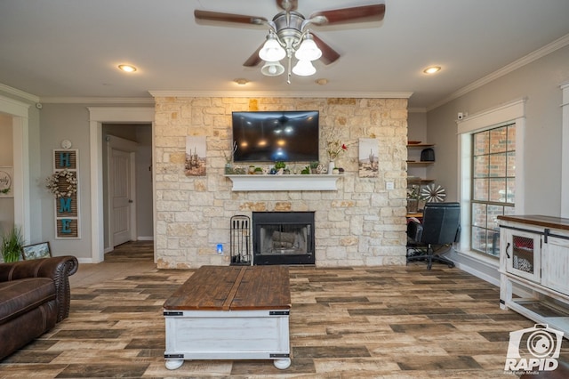 living room with ornamental molding, a stone fireplace, hardwood / wood-style floors, and ceiling fan