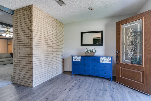 foyer entrance with ceiling fan, wood-type flooring, a textured ceiling, and brick wall