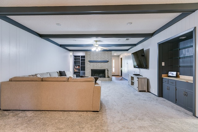 living room with a fireplace, beam ceiling, light colored carpet, ceiling fan, and a textured ceiling