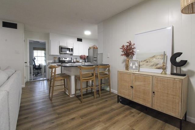 kitchen with a breakfast bar area, stainless steel appliances, white cabinets, dark hardwood / wood-style flooring, and kitchen peninsula