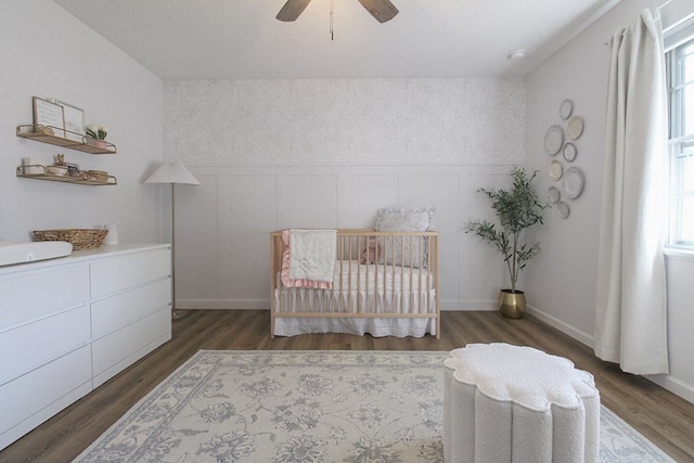 bedroom with ceiling fan, dark hardwood / wood-style floors, and a crib