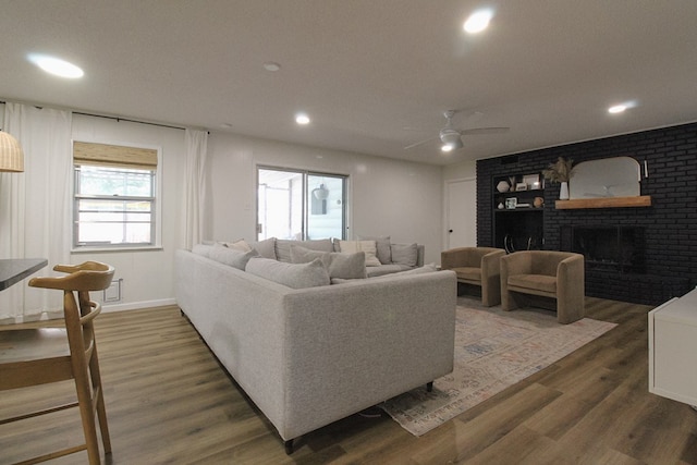 living room with a brick fireplace, dark hardwood / wood-style floors, and ceiling fan