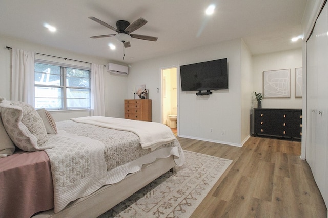 bedroom with ensuite bathroom, hardwood / wood-style floors, ceiling fan, and a wall unit AC