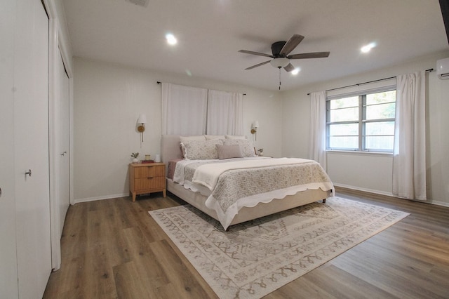 bedroom with ceiling fan, hardwood / wood-style floors, and an AC wall unit