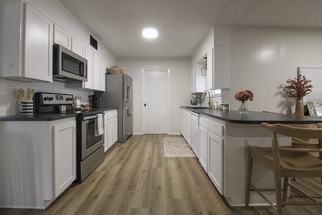 kitchen with sink, a breakfast bar area, white cabinetry, hardwood / wood-style floors, and stainless steel appliances