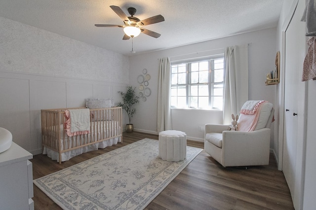 bedroom with a crib, dark hardwood / wood-style floors, a textured ceiling, and ceiling fan