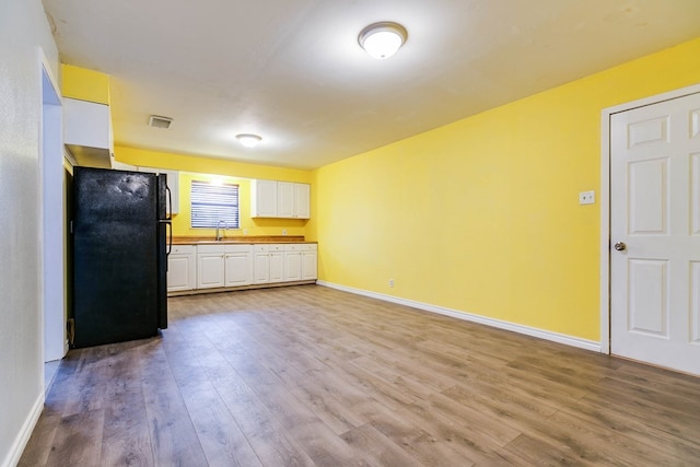 kitchen featuring black refrigerator, white cabinetry, light hardwood / wood-style flooring, and wooden counters