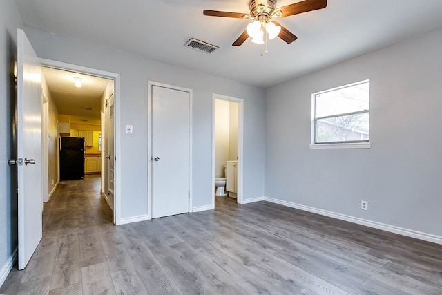 unfurnished bedroom with black refrigerator, connected bathroom, light hardwood / wood-style flooring, ceiling fan, and a closet