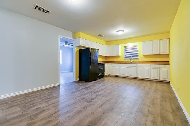 kitchen with white cabinetry, sink, stove, black fridge, and light hardwood / wood-style flooring