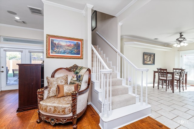 stairs featuring wood finished floors, visible vents, ornamental molding, and ceiling fan