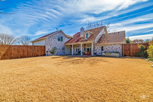 back of house featuring stone siding, a chimney, fence, a patio, and a lawn
