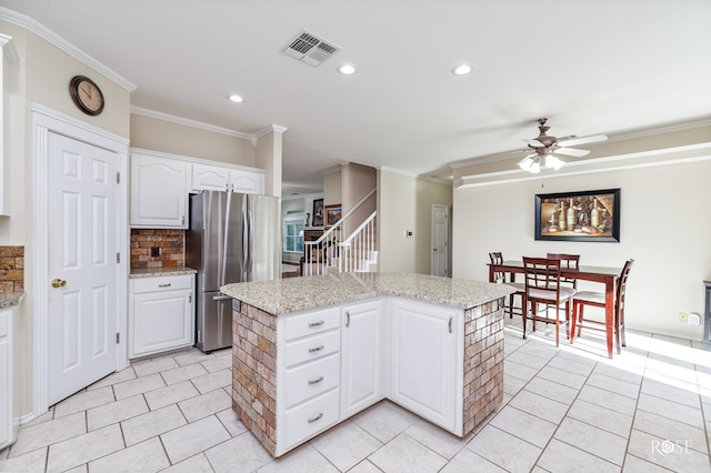 kitchen with crown molding, a center island, ceiling fan, freestanding refrigerator, and visible vents