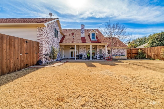 back of house with a fenced backyard, a lawn, a chimney, and a patio