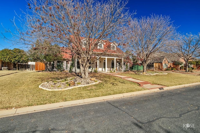 view of property hidden behind natural elements featuring covered porch, a front yard, and fence
