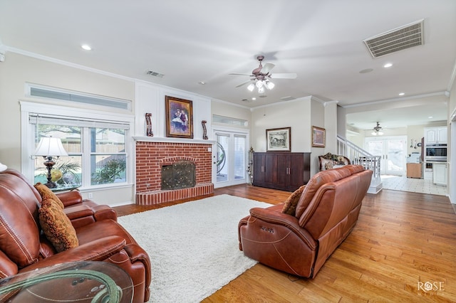 living room featuring visible vents, ornamental molding, light wood-type flooring, and a ceiling fan