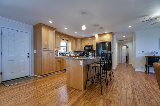 kitchen with black refrigerator, decorative light fixtures, a kitchen breakfast bar, a center island, and light wood-type flooring