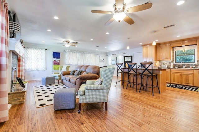 living room with ceiling fan, ornamental molding, sink, and light hardwood / wood-style floors