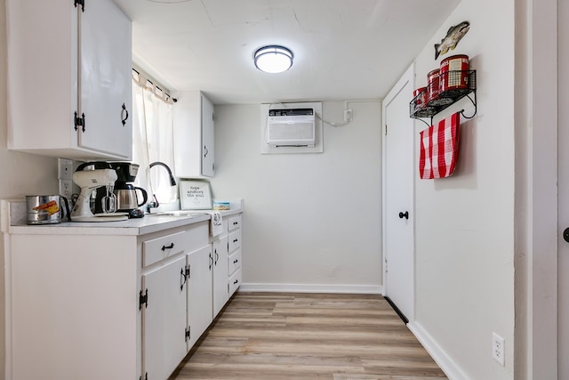 kitchen featuring sink, a wall mounted AC, white cabinets, and light hardwood / wood-style flooring