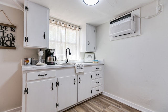 kitchen featuring white cabinetry, an AC wall unit, sink, and light hardwood / wood-style flooring