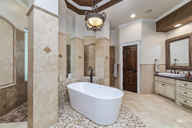 bathroom featuring a bath, tile walls, crown molding, vanity, and ornate columns