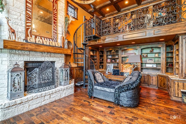 living room featuring a high ceiling, dark wood-type flooring, a stone fireplace, and coffered ceiling