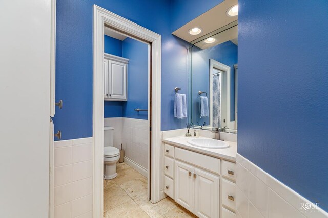 bathroom with toilet, tile walls, tile patterned flooring, and vanity