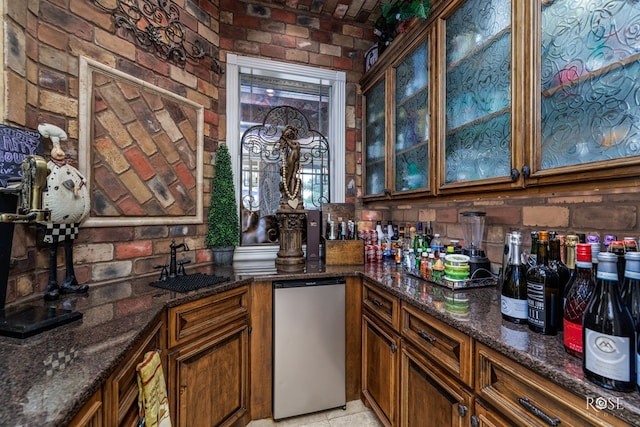 bar featuring brick wall, sink, dark stone countertops, and stainless steel fridge