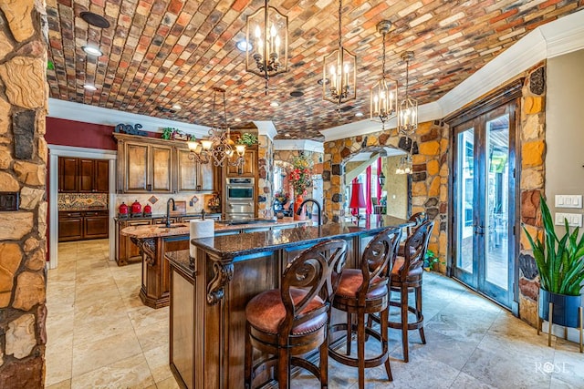 kitchen featuring an island with sink, french doors, dark stone counters, and pendant lighting