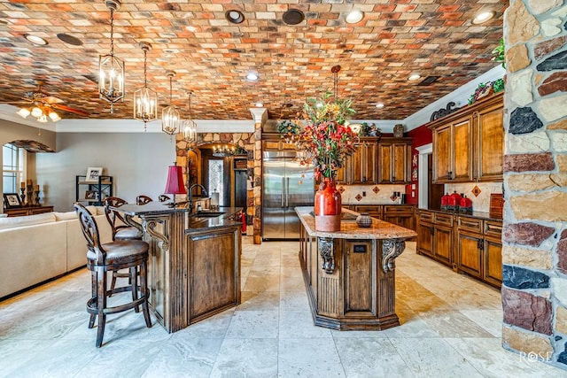 kitchen with a breakfast bar, built in fridge, decorative light fixtures, crown molding, and a kitchen island with sink