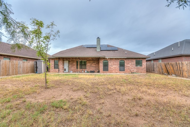 back of property with a lawn, a shed, and solar panels