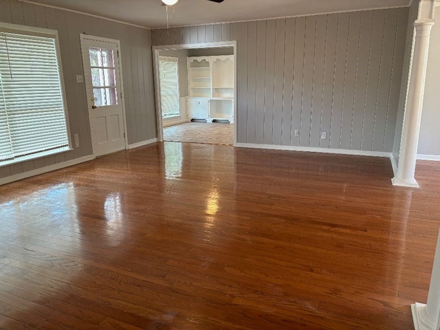 empty room featuring hardwood / wood-style flooring, ceiling fan, wood walls, and ornate columns