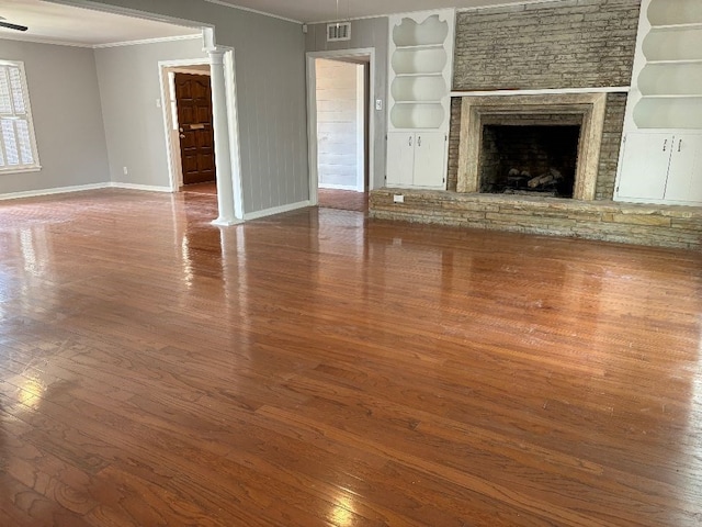 unfurnished living room featuring crown molding, hardwood / wood-style floors, built in shelves, and a stone fireplace