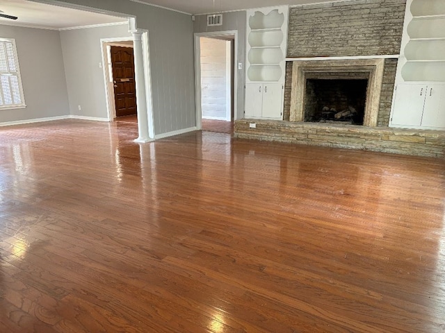 2661 Oxford Ave, San Angelo, TX 76904 - unfurnished living room featuring crown molding, hardwood / wood-style floors, built in shelves, and a stone fireplace