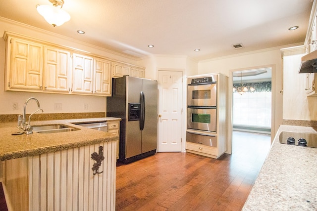 kitchen featuring appliances with stainless steel finishes, hardwood / wood-style floors, sink, ornamental molding, and light stone counters