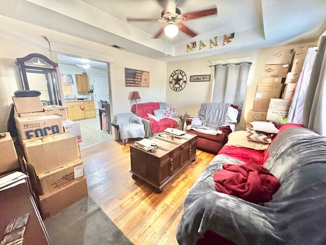 living room featuring ceiling fan, a tray ceiling, sink, and light wood-type flooring