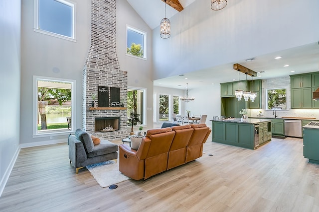 living room featuring sink, a high ceiling, a fireplace, a chandelier, and light wood-type flooring