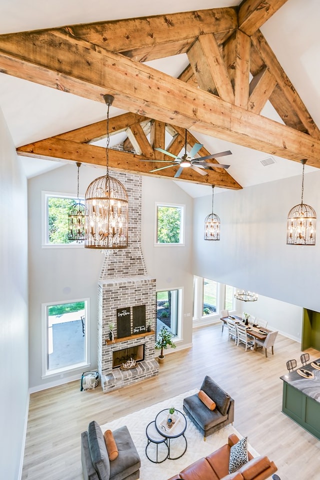 living room featuring ceiling fan with notable chandelier, high vaulted ceiling, wood-type flooring, a brick fireplace, and beam ceiling