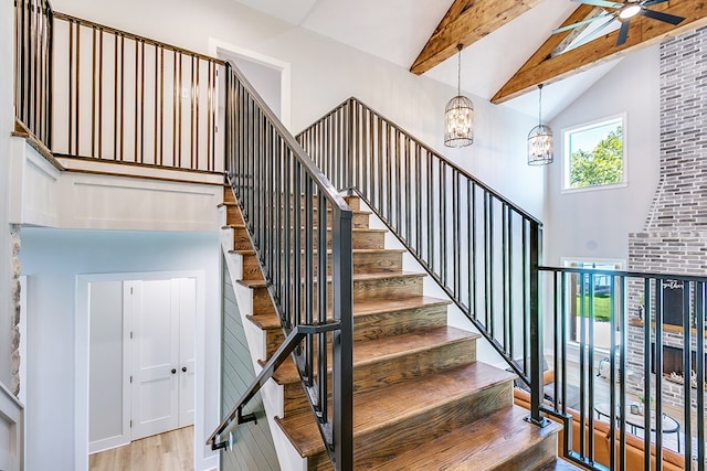 stairway with wood-type flooring, ceiling fan with notable chandelier, and vaulted ceiling with beams