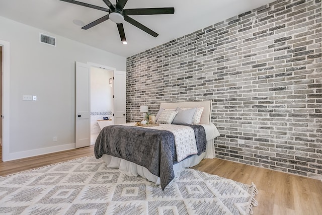 bedroom with ceiling fan, brick wall, and light hardwood / wood-style floors