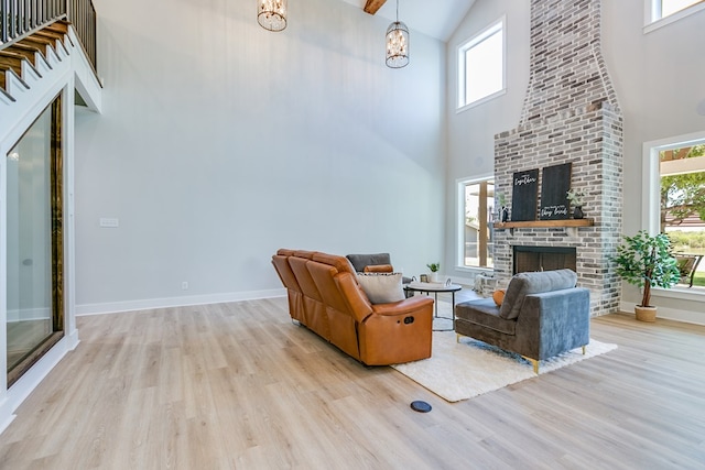 living room with a towering ceiling, plenty of natural light, a fireplace, and light wood-type flooring