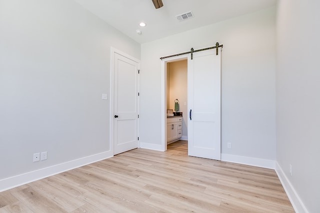 unfurnished bedroom featuring connected bathroom, a barn door, ceiling fan, and light wood-type flooring