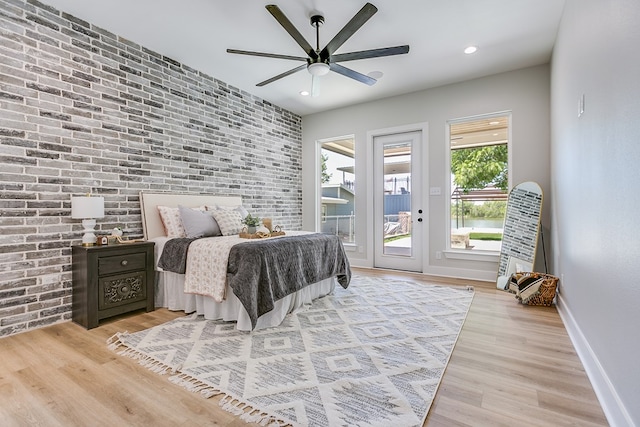 bedroom featuring access to exterior, light wood-type flooring, ceiling fan, and brick wall