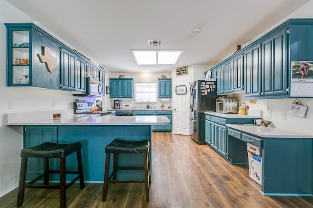 6038 Winners Cir, San Angelo, TX 76904 - kitchen with a peninsula, appliances with stainless steel finishes, blue cabinets, dark wood finished floors, and light countertops