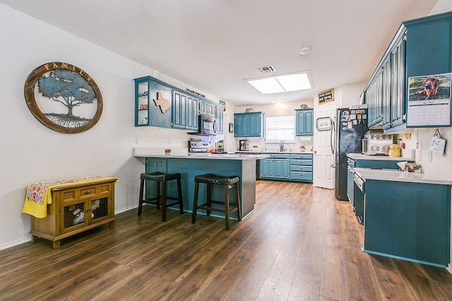 6038 Winners Cir, San Angelo, TX 76904 - kitchen featuring blue cabinetry, stainless steel appliances, a peninsula, dark wood-style floors, and a breakfast bar