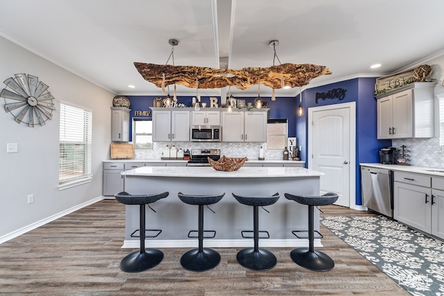 kitchen featuring gray cabinets, appliances with stainless steel finishes, hanging light fixtures, a center island, and crown molding