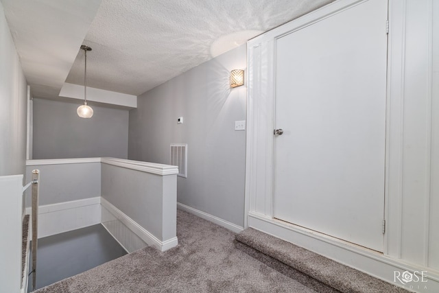 stairway featuring a textured ceiling and carpet