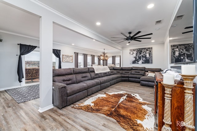 living room with ceiling fan with notable chandelier, ornamental molding, and light hardwood / wood-style floors